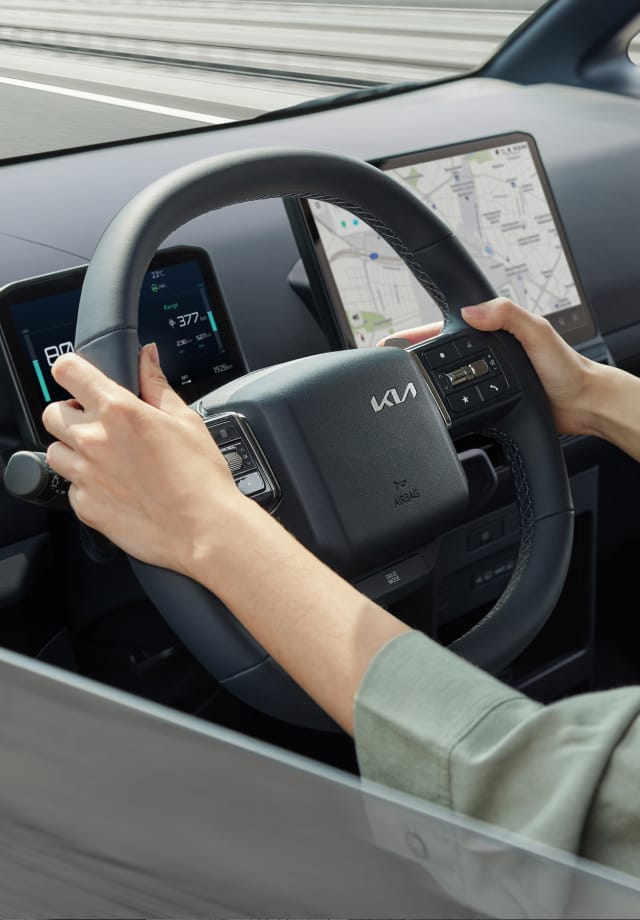 Nahaufnahme des Fahrers, der das Lenkrad des Kia PV5 Passenger hält.